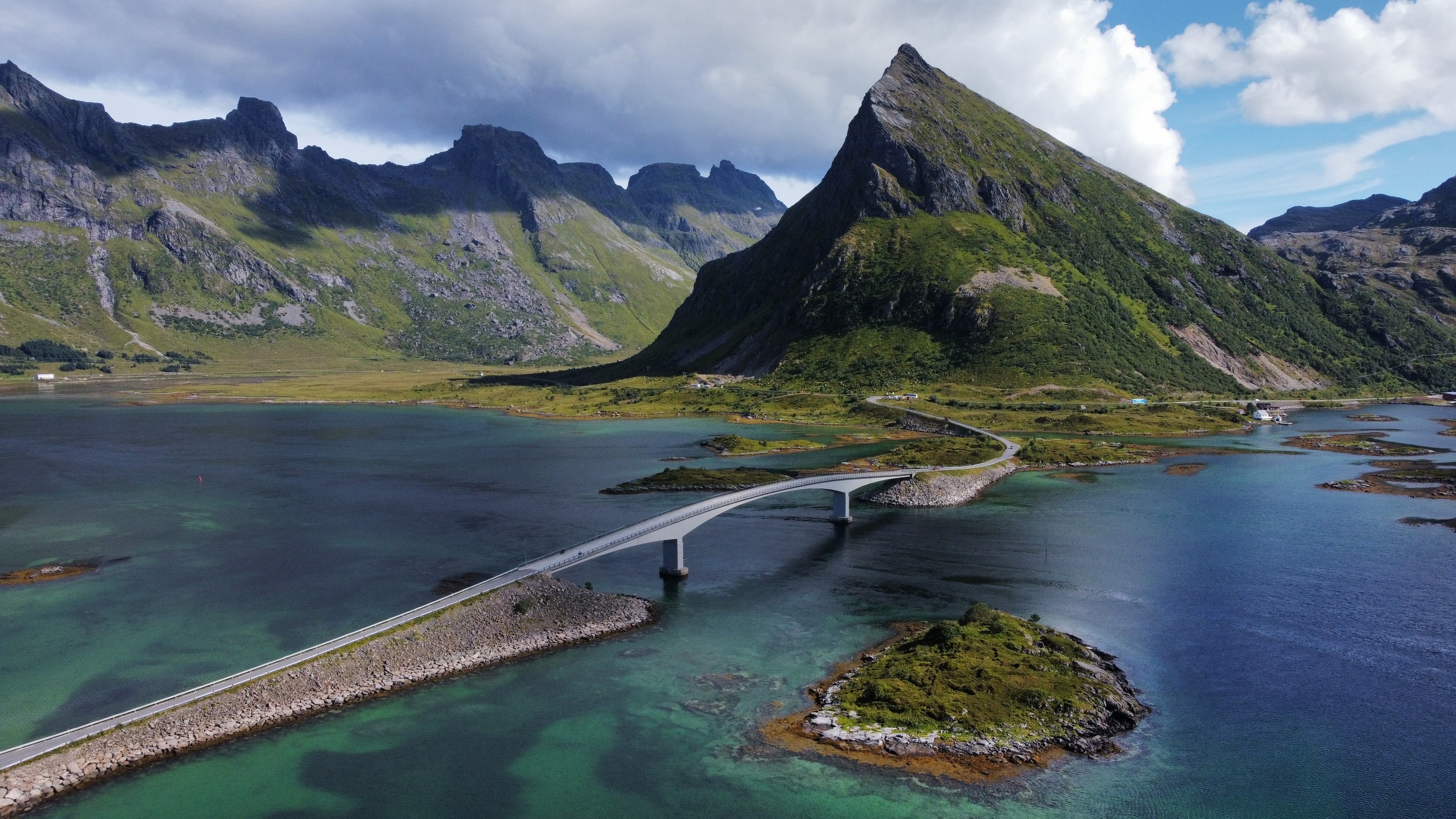 Dramatic green mountain peaks and a bridge over clear coastal water